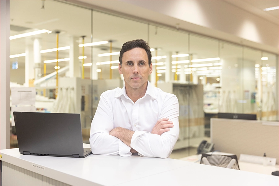 Nicholas sits on desk with laptop, arms folded